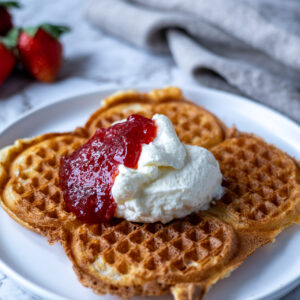 våffla på tallrik med vispad grädde och jordgubbssylt