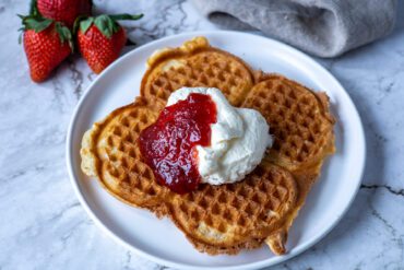 våffla på tallrik med vispad grädde och jordgubbssylt